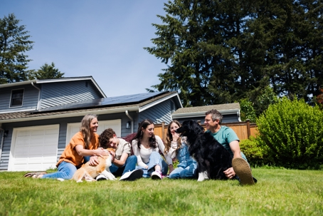 Family In Front Yard With Dogs and Solar Equipped Home
